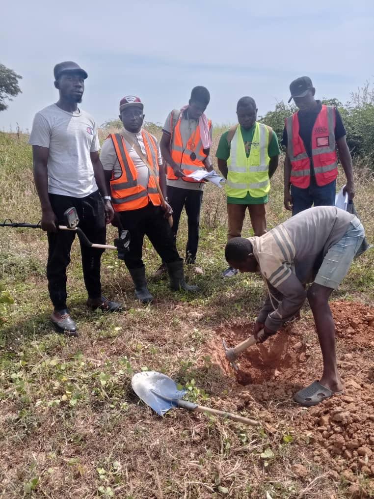 Team gathered around a test pit as a sample is extracted for inspection.